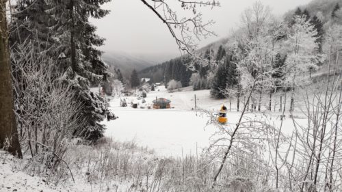 Skipiste Meva mit Schnee Erzeugern, dahinter Bäume verschneit
